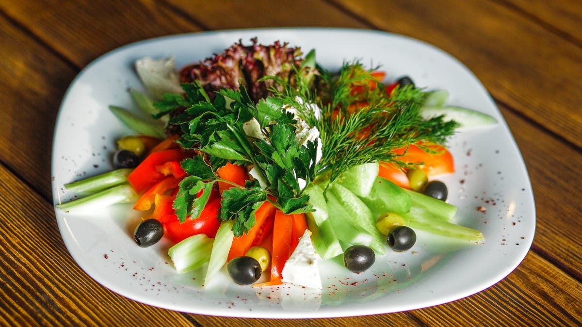 Colorful vegetable salad with fresh herbs and black olives on a white plate.